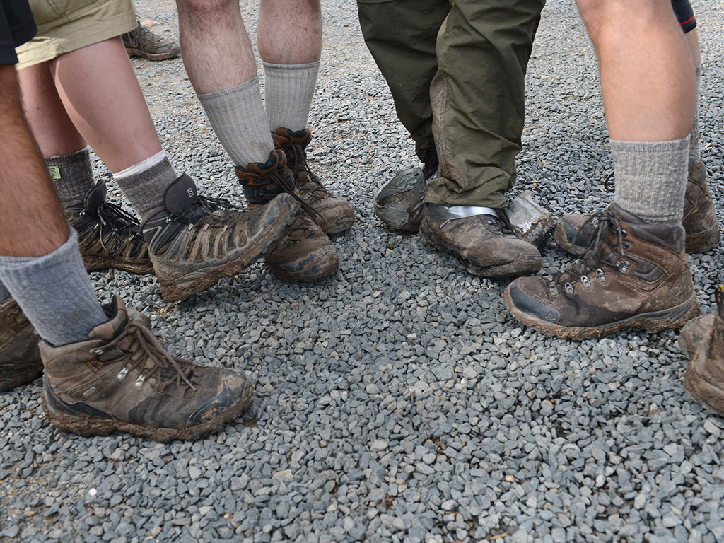 Men showing off their muddy boots in a circle